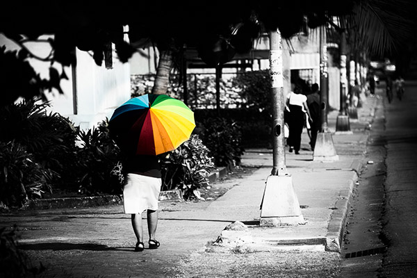 Woman walking with rainbow umbrella down street